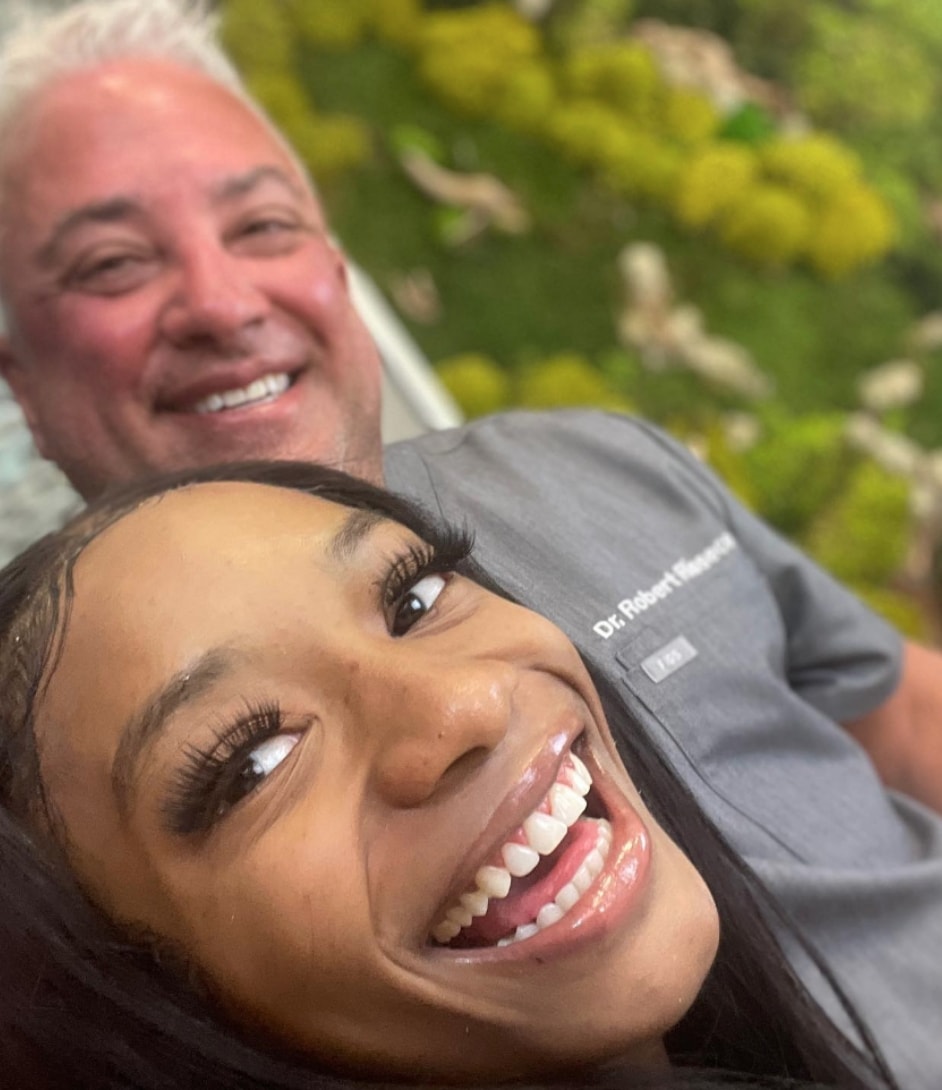 A patient smiling at the camera with Dr. Rioseco in the background